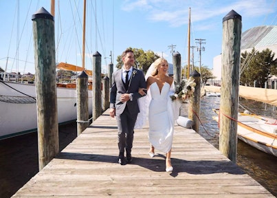 Nichole Pellegrino and Michael Freas wearing a Generation Tux suit walking along a doc arm in arm.