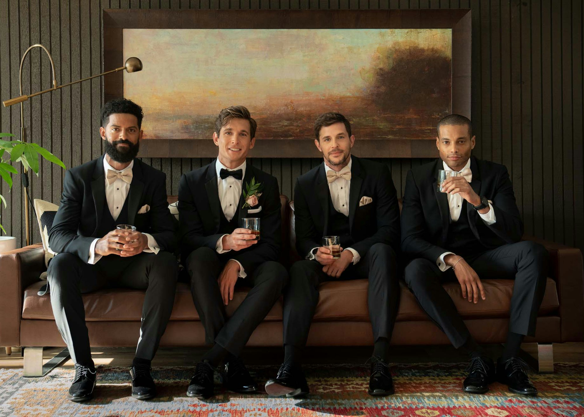 Photo of four groomsmen with drinks on a couch wearing Black Peak Lapel Tuxedos