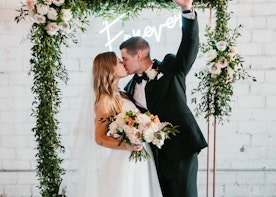 Bride and groom kissing in front of floral arch