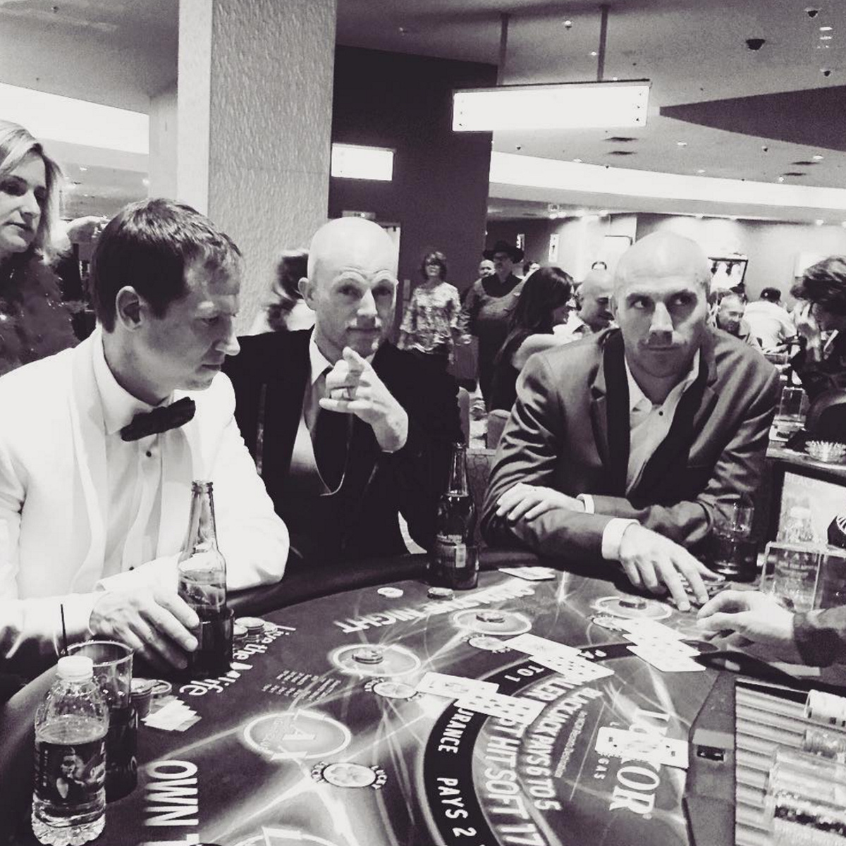 Black and white photo of 3 guys in suits sitting at a poker table.