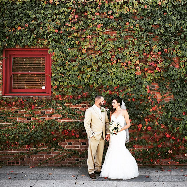 Bride and groom in front of a vide covered brick wall outside.