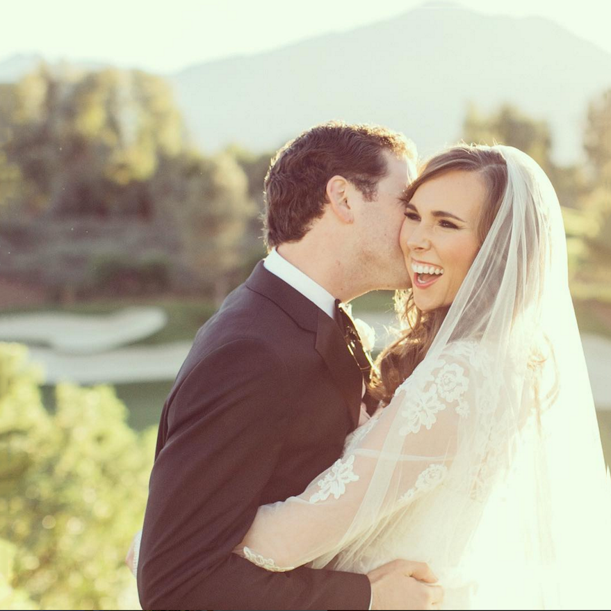 Groom kissing his bride outside on a sunny day.