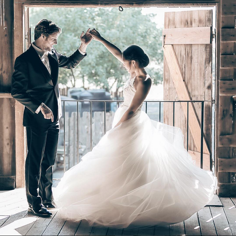 Groom spinning a bride in a bard with the sunny outdoors as a backdrop.