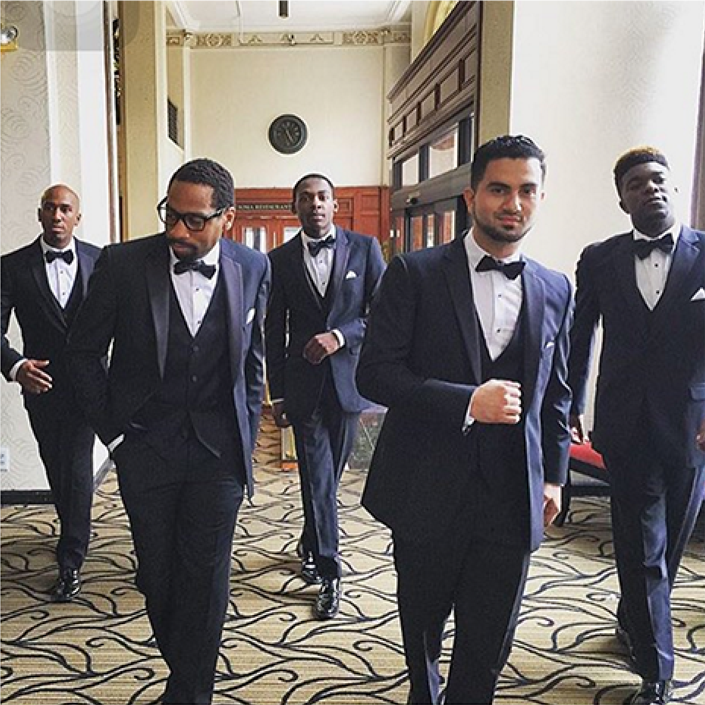 Groomsmen walking cool down a hallway in black suits.